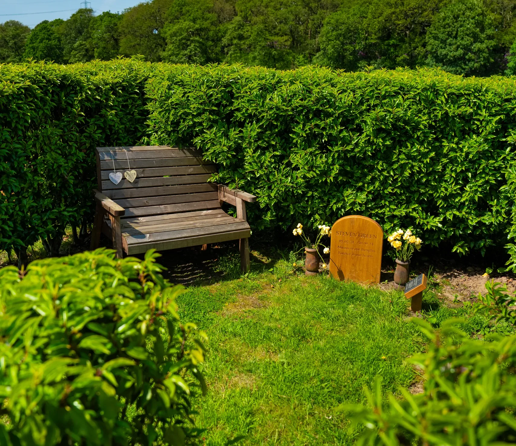 A private Living Memorial Garden with neatly trimmed hedges, a memorial bench and headstone in peaceful landscaped surroundings.